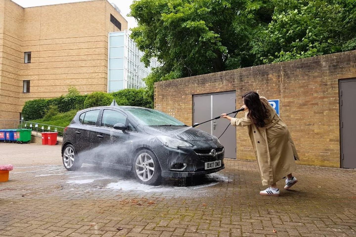 Person washing a black car with a power hose outside a building